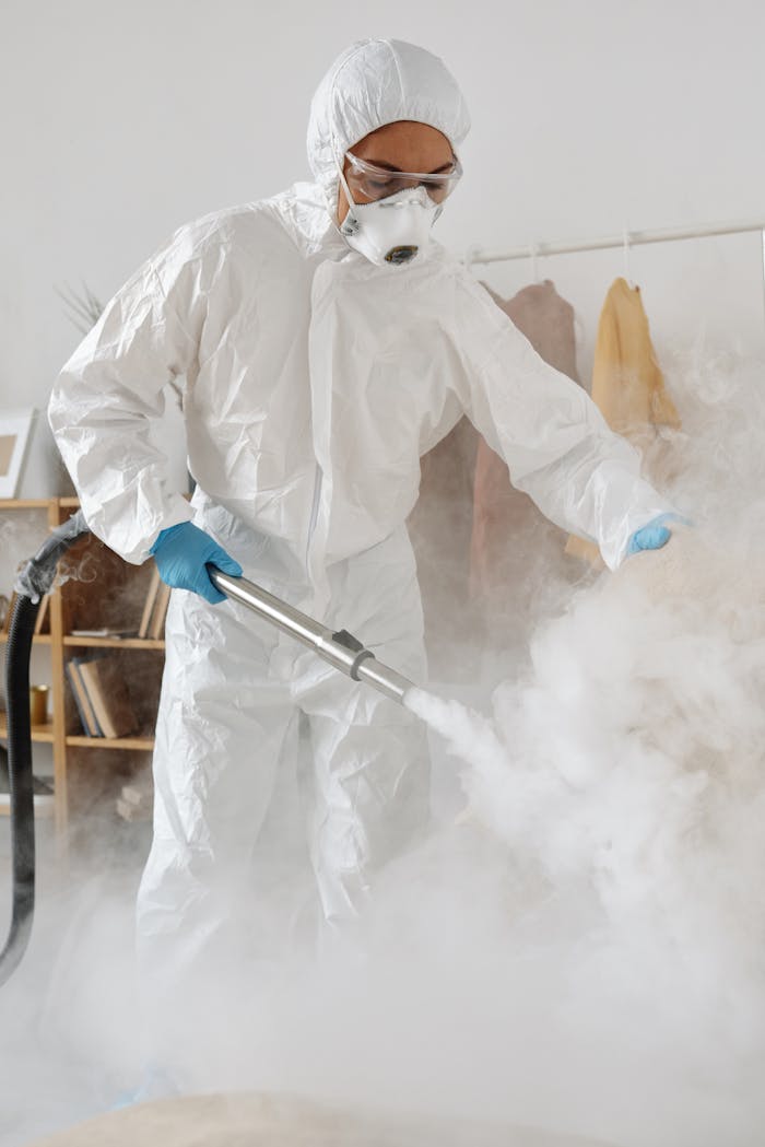 Person in PPE fumigates indoors with protective suit, gloves, and mask.